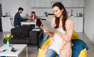 Una chica navega por una tableta en primer plano. En segundo plano, desenfocados, hay una pareja trabajando sobre una mesa.  