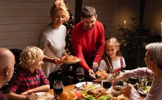 Una familia disfruta de la cena de navidad. Se ve a los padres de pie sirviendo la comida al resto de la familia.