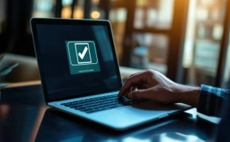 Una pantalla de ordenador, muestra un simbolo de aprobación mientras una mano de hombre descansa sobre el teclado.