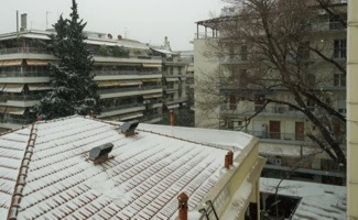 Vista de edificios residenciales con tejados cubiertos de nieve durante una nevada, mostrando un entorno urbano en invierno.
